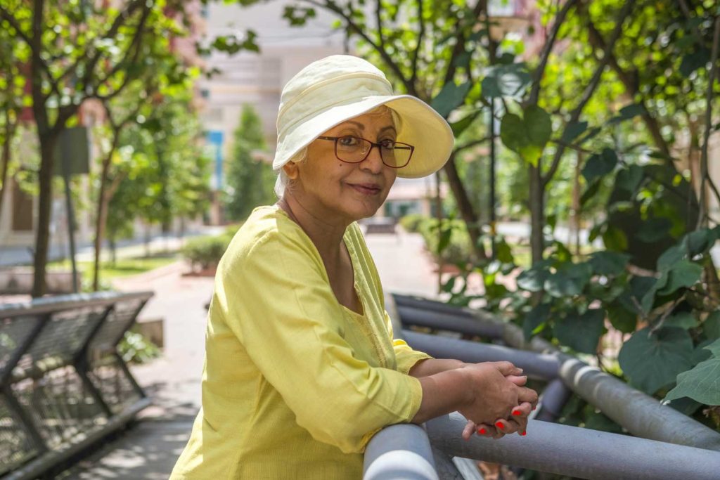 Women of and older 50 can start fashion trends. The woman depicted here is wearing a sunhat and a quarter length sleeve shirt, softly smiling.