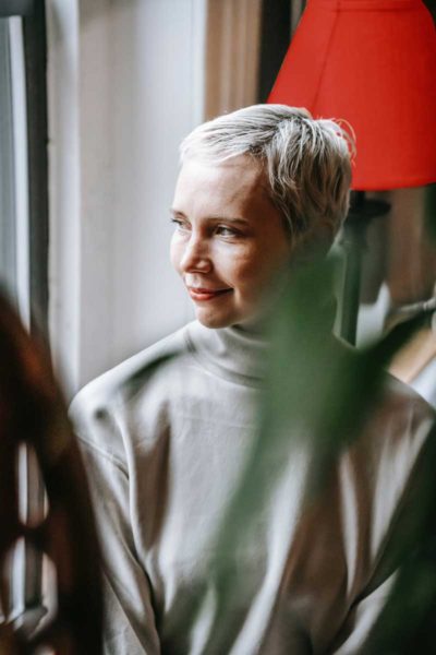 This younger woman has dyed her hair white and she's wearing a turtle neck shirt, looking out of a window.